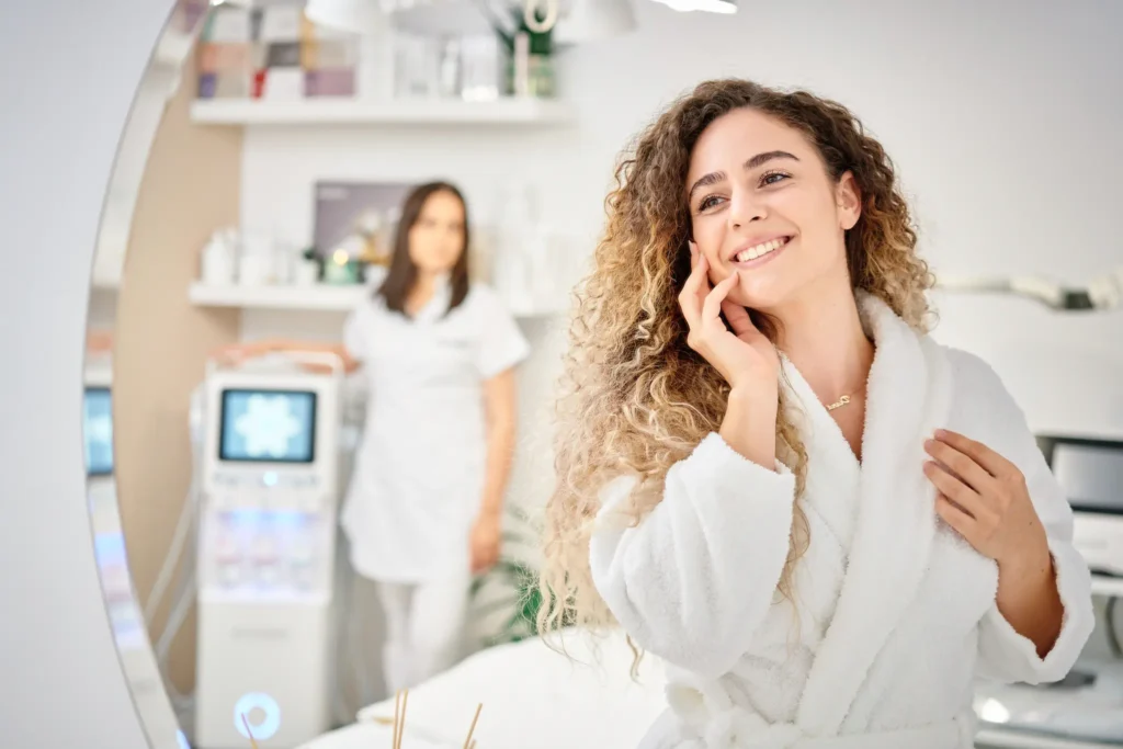 A woman in a green scrub suit is treating client's face with a machine.
